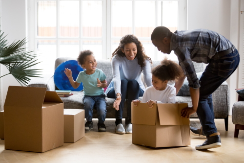 This image: a young family are smiling and unpacking boxes in an empty, sunlit room. The map: an illustrative housing layout has appeared over the site, with interactive information markers which describe the design elements in more detail. The local conservation area adjacent to the site is highlighted.